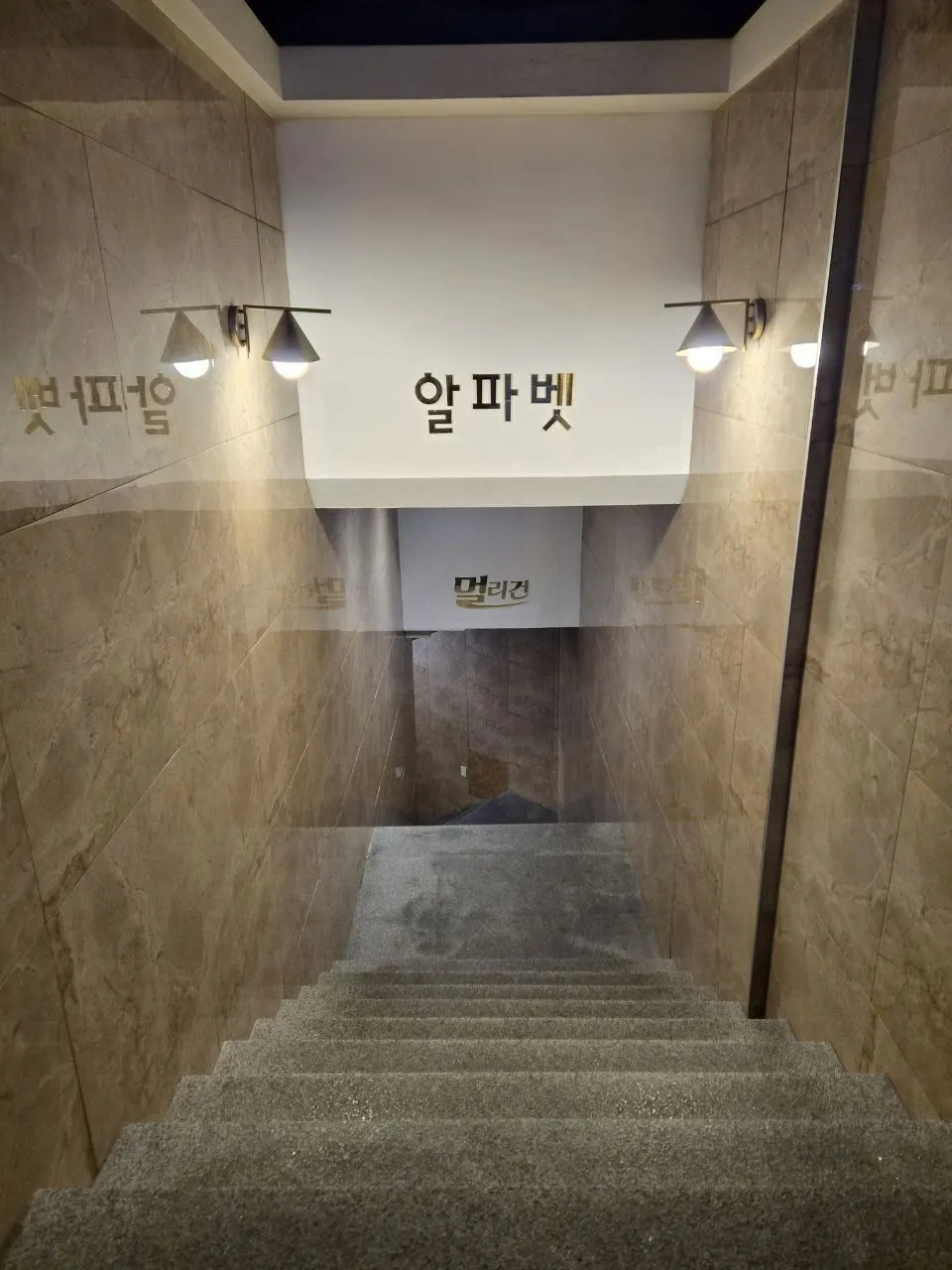 강남 멀리건으로 내려가는 실내 계단. 벽면 조명 아래 알파벳과 멀리건 사인이 보인다