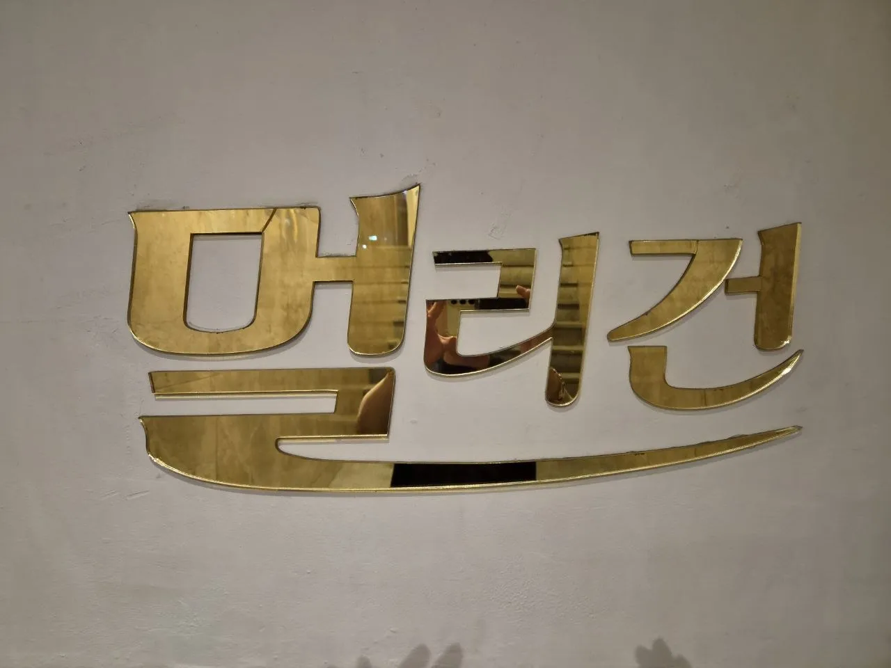 벽에 붙은 강남 멀리건 금색 로고를 가까이 촬영한 사진