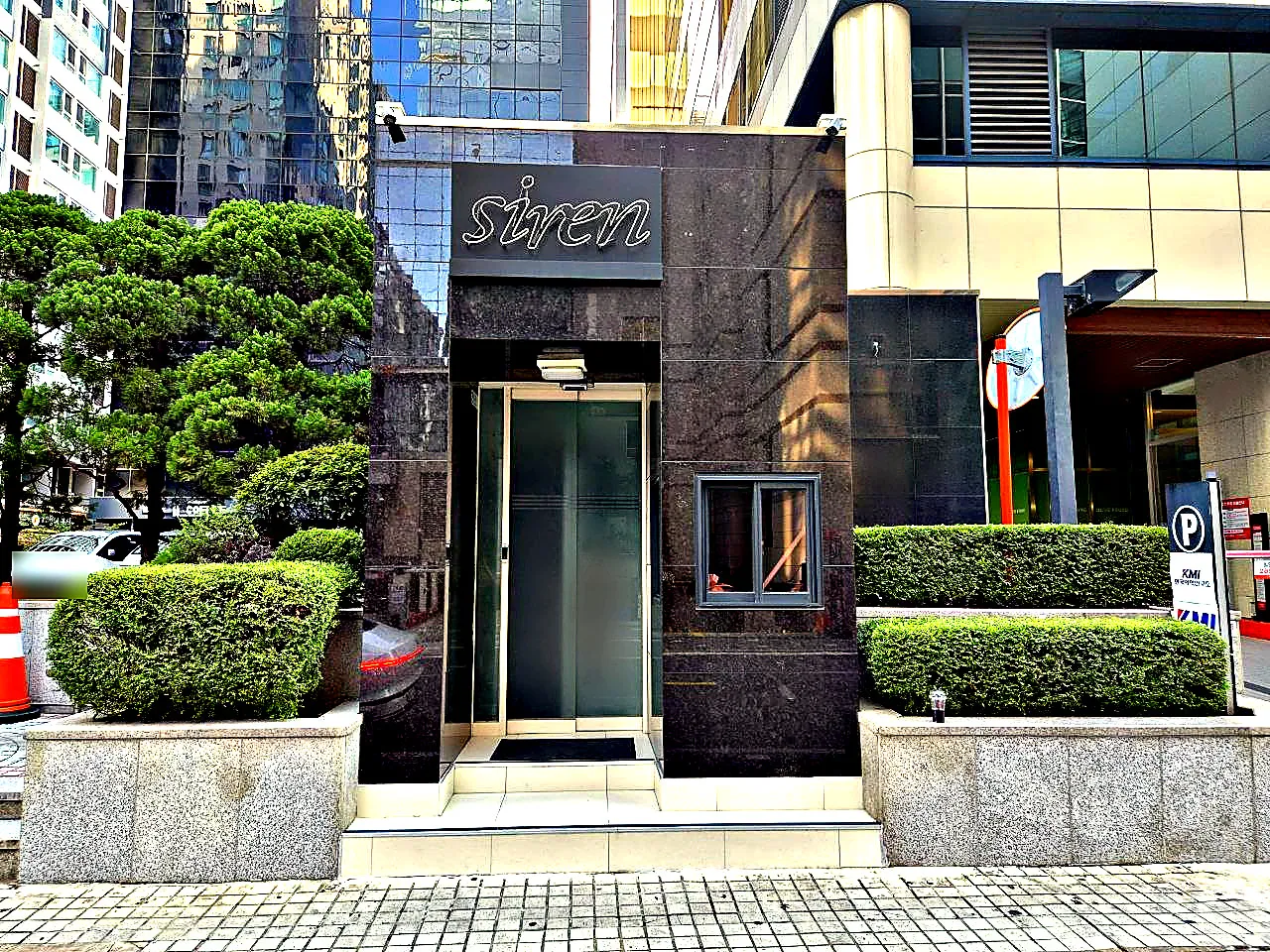siren 이라고 쓴 강남 세이렌 간판이 달린 건물 출입구와 주변 화단이 함께 보이는 사진